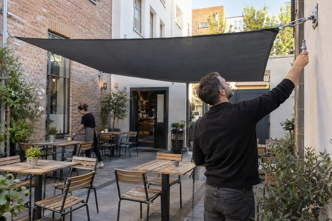 Gastronom prüft die Spannung eines Sonnensegels über einer Caféterrasse