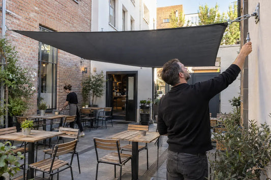 Gastronom prüft die Spannung eines Sonnensegels über einer Caféterrasse